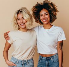 photo of blonde short hair woman and latin curly hair woman wearing white *t-shirt mockup* and jeans, cheerful, arm around each other, blonde woman open hand to left side, isolated on off white background, real authentic people --v 6.0 --ar 3:2