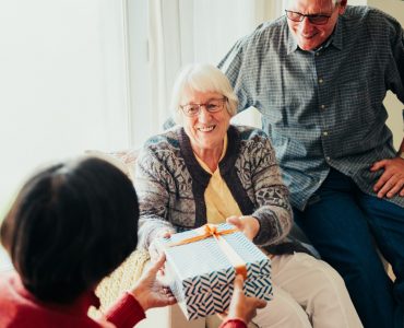 Elderly Indian woman receiving a gift from another elderly woman with an elderly man nearby. Gift exchange in retirement home. Diverse elderly women and elderly man in retirement home together.