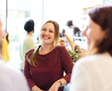 Happy Caucasian woman smiling in a cafe. Bright atmosphere in the cafe, with people in the background. Happy woman enjoy talking with her friends at cafe. Woman listening to friends at coffee shop