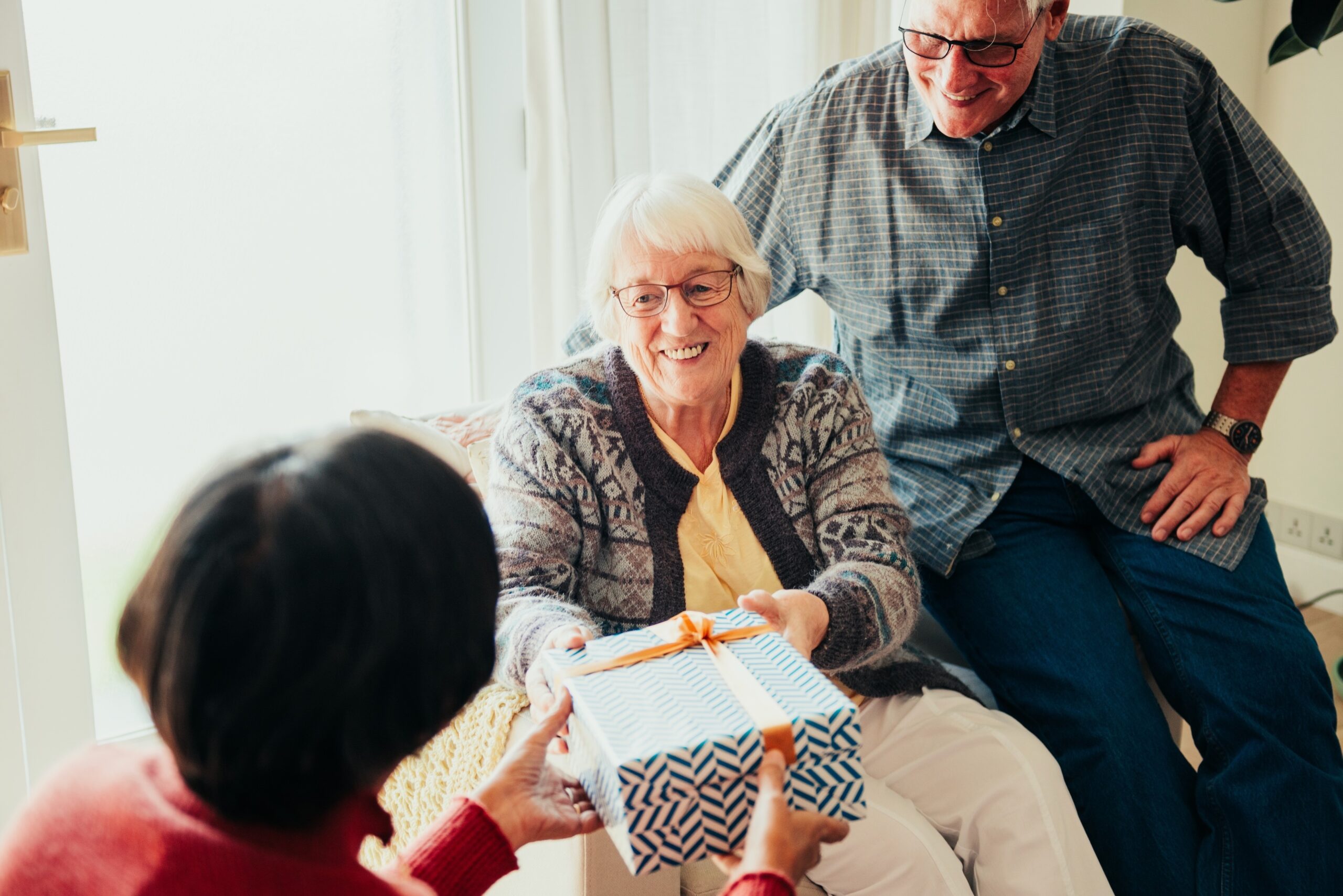 Elderly Indian woman receiving a gift from another elderly woman with an elderly man nearby. Gift exchange in retirement home. Diverse elderly women and elderly man in retirement home together.