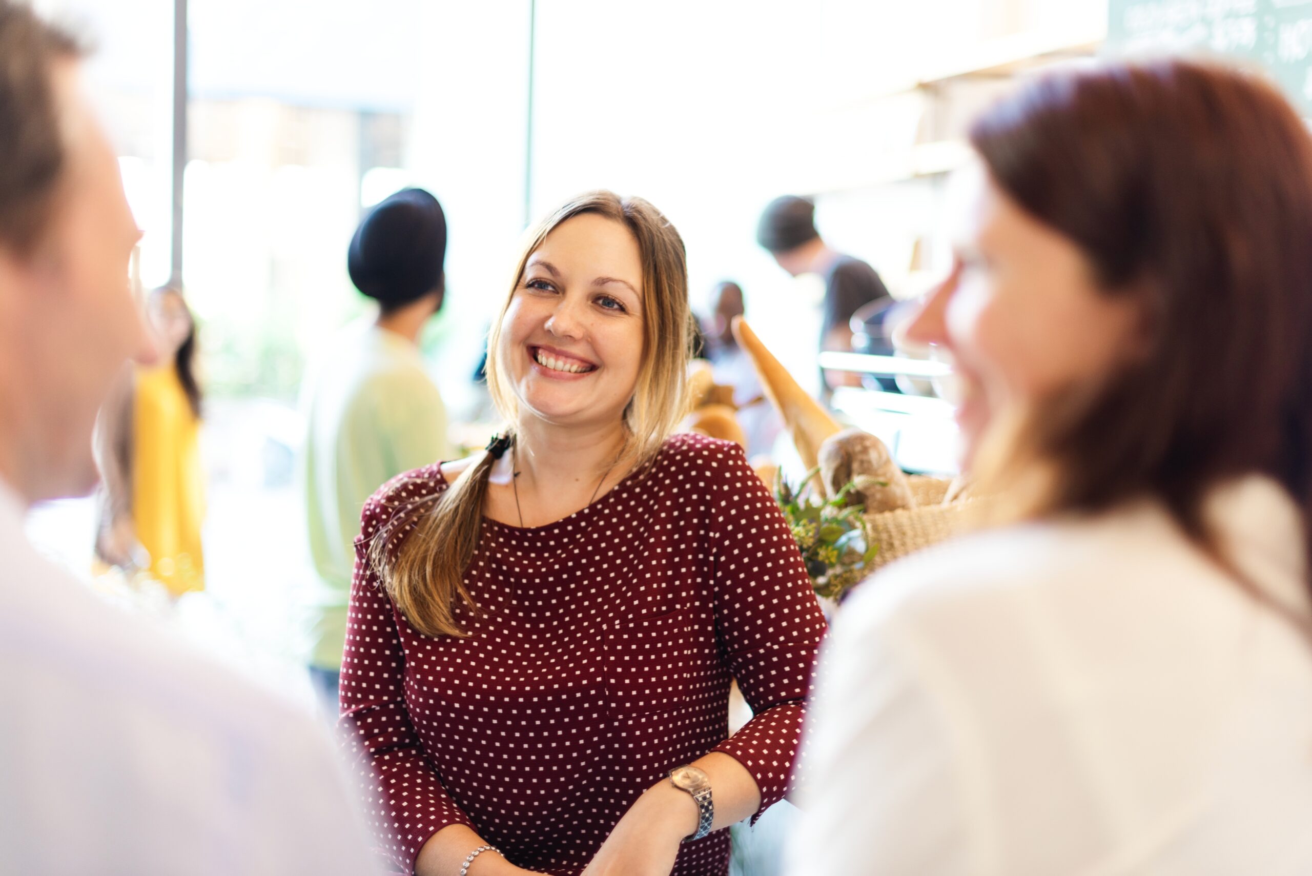 Happy Caucasian woman smiling in a cafe. Bright atmosphere in the cafe, with people in the background. Happy woman enjoy talking with her friends at cafe. Woman listening to friends at coffee shop